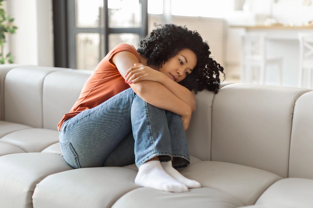 Portrait of depressed black woman sitting on couch at home
